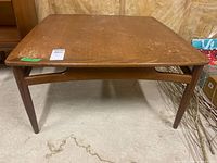 Front view of vintage teak coffee table on concrete floor showing surface watermarks and visible wear.