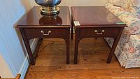 Pair of Thomasville cherry side tables with brass drawer handles and polished tops placed on wooden floor next to floral couch.