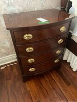 Front angled view of the dresser showing all four drawers with oval brass handles and wood grain.