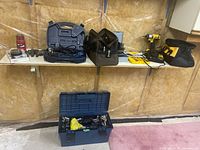 Full view of lot showing tools on shelf and on floor: blue toolbox with socket set, black vice clamp, Mastercraft rotary tool in blue case, DeWalt drill charger and bag, other small tools and drill bits.