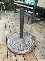 Photo of the full umbrella stand showing circular ribbed base and pole on a wooden deck