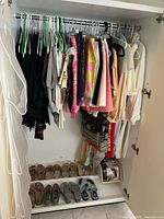 Photo of closet with hanging women's clothing including pants, skirts, dresses, tops in various colors and shoes on bottom shelf in various styles and colors