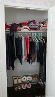 Closet view showing hanging women's pants, jeans, and shorts with folded tops arranged on upper shelf.