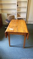 Front view of antique pine drop leaf table with leaves extended showing natural cracks and wood grain.
