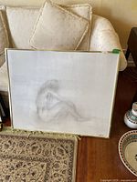 Photo showing the full canvas painting of a seated nude woman in a frame with the setting in a living room area.