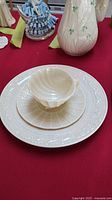 Photo of Belleek porcelain cup, saucer, and plate arranged stacked on a red surface, highlighting embossed design details.