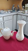 Photo of Belleek daisy vase and teapot on red surface, showing both items side by side