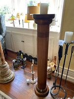 Full view of wooden candle holder with white pillar candle on top, located indoors on wooden floor near window.