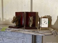 Overall view of clock and two brass horse head bookends on marble surface