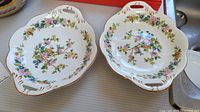 Two oval porcelain dishes with floral decoration and gold accents shown side by side