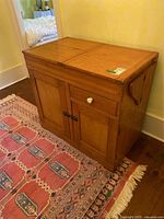 Full view of wood dry sink closed, showing flat top with two folding side wings, wood finish and drawer and door fronts.