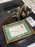 Photo showing seven small metal figurines arranged on a black surface with one framed artwork in foreground