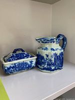 Blue and white Flow Blue style butter dish with lid and matching pitcher on display shelf.