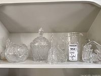 Front view of the glass and crystal items displayed on a shelf including the bell, nativity glass art, napkin holder, serving dishes and pitcher.