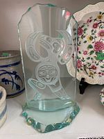 Full view of the glass sculpture showing the overall shape and etched design on the front.