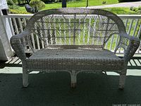 Front view of outdoor wicker love seat showing woven lattice design with damage and fraying.