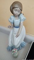 Front view of Nao by Lladro porcelain figurine of girl with small flower vase in front.
