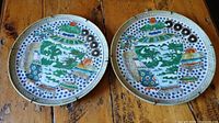 Two ceramic plates side by side on wood table showing colorful Asian-inspired pattern and noticeable chips.