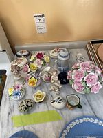 Wide view of collection on marble tabletop showing multiple porcelain flower arrangements, pitchers, trinket dishes, and figurines.