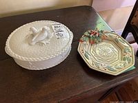 Royal Worcester white ceramic covered dish with bird handle on lid and octagonal Fitz and Floyd holiday-themed plate on a wooden table.