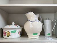 Photo showing three white ceramic items on shelf: floral Royal Worcester Pershore serving dish with lid, ceramic pitcher with ornate embossed design, and vertical ribbed Arzberg coffee pot with lid.