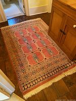 Full view of rectangular rug on wood floor showing central medallion pattern, multiple borders, and fringe at near end