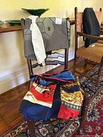 Scarves draped over a wooden chair showing various colors and patterns, including multi-color carriage and ornamental design, gray house pattern scarf, and a white scarf.