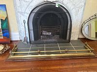 Fireplace area with brass fender in front on floor, fireplace screen set against fireplace, ash shovel nearby