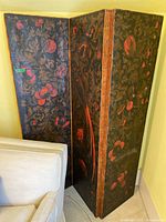 View of the entire three-panel folding screen angled showing floral canvas panels and wooden frame with nailhead trim.
