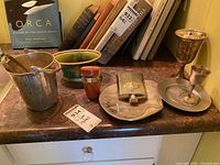 Photo of ice bucket, goblets, shot glasses in case, decorative bowl on marble surface with books in background