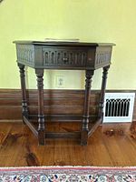 Front view of the wood hall table showing one drawer and turned legs on a wooden floor with baseboard and heating vent behind