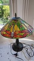 Full view of lamp showing metal base and stained glass style shade with dragonfly designs