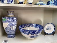 Blue and white ceramic bowl, vase, and decorative plate arranged on shelf