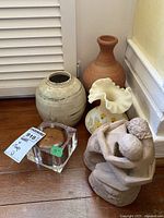 Photo of five items grouped on the floor including a glass candle holder with a brown candle, two pottery vases, the Fenton vase with ruffled edges and floral decoration, and the clay figure sculpture.