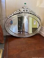 Vintage oval mirror resting on wooden floor against a wall, showing the whole front view with beveled glass and decorative frame.