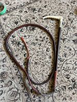 Full view of whip showing cream bone curved handle, metal collar and long braided leather lash on patterned carpet.