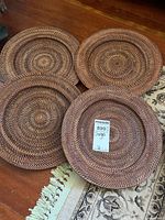 Four hand woven chargers laid on wooden floor showing textured spiral woven design in various shades of brown.