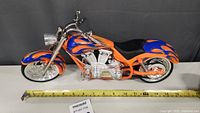 Side view of model motorcycle measuring about 16 inches long, showing orange body with blue flames and chrome silver details.