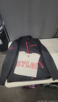 Photo of black Spyder jacket with red zipper accents and white T-shirt with red lettering placed on a flat surface.