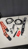 Full lot showing guitar straps, guitar cables, guitar picks, small hammer, and small accessories on white table.