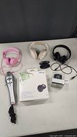 Three pairs of headphones (pink wired, beige wireless, black wired), wireless microphone and Nokia earbuds in box with charging case on table