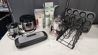 Photo showing all small kitchen appliances and accessories grouped together including vacuum sealer, rice cooker, blender, stockpot, pan rack, muffin pan, spice rack, and food saver rolls.