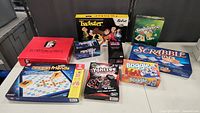 Photo showing all nine family board games together on a table including Scattergories, Twister Retro, Sequence, Scrabble Tile Game, Words With Friends, Mindware Mindwarp, Yahtzee, and two Boggle games.