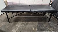 Full view of the unfolded black padded portable massage table with face cradle cutout, showing the table top and metal legs.