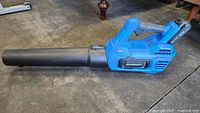 Mastercraft blue 20V cordless leaf blower laying on carpet, side view showing blower tube and handle.