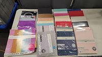 Photo showing multiple sealed packages of assorted colors and sizes of card stock paper laid out on a table.