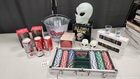 Full lot view showing Alien bank, poker chip set, Coors Light bucket, soda cans, skull shot glasses, shaker set, Coca-Cola collectibles