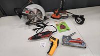 Photo of the entire power and hand tools lot showing the circular saw, cordless drill, rotary engraver tool, staple gun, and heat gun arranged on a table.