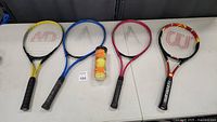 Four tennis rackets laid out with three tennis balls in a canister placed on a table