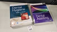 Two dental textbooks placed on a surface with visible covers: 'Dental Hygiene Theory and Practice, Fourth Edition' and 'Modern Dental Assisting'.